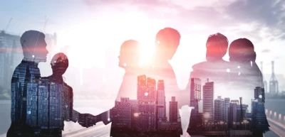 Silhouetted businesspeople shaking hands with a city skyline overlaid, symbolizing partnership and collaboration.