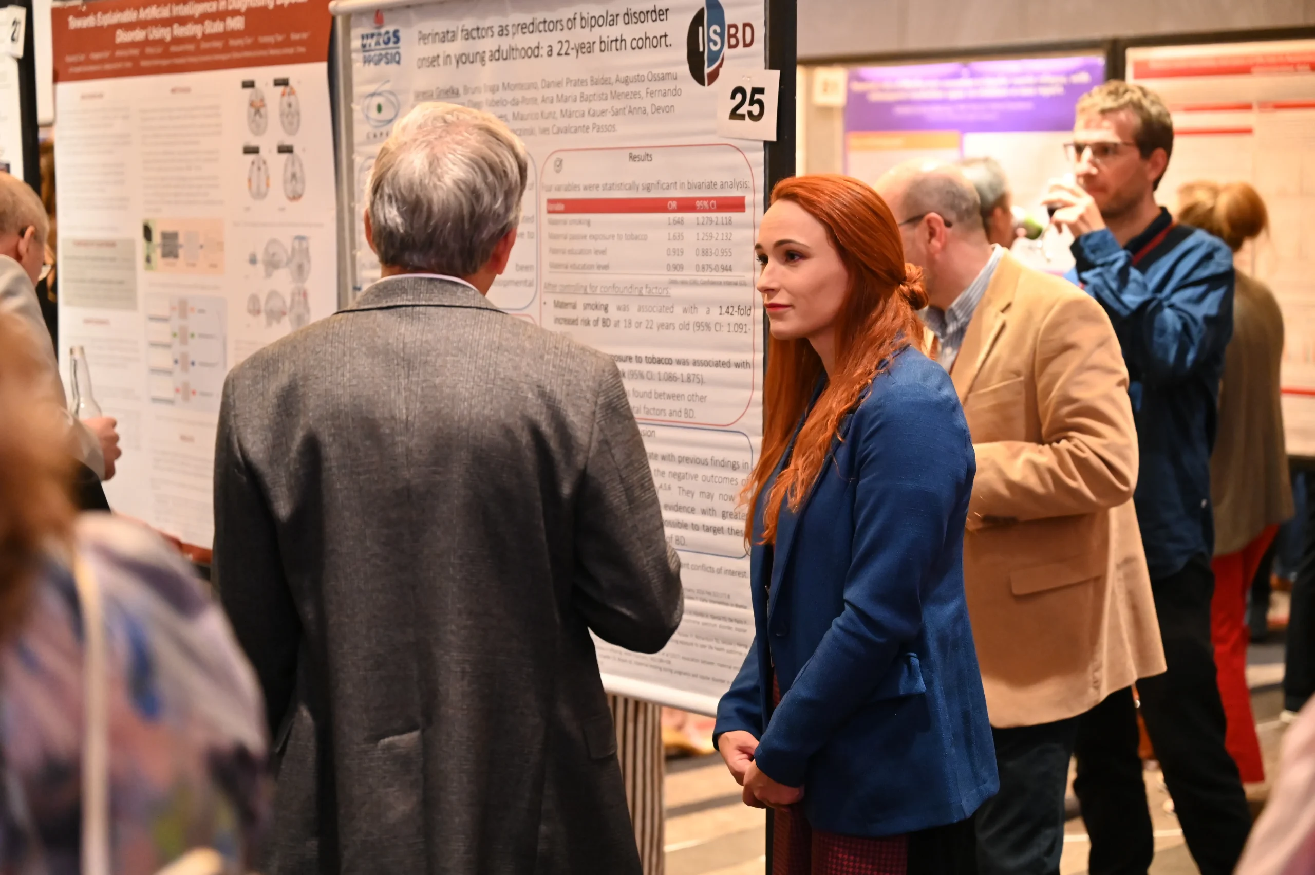 Group of people at a poster session studying a large research poster with charts and text, in a busy conference hall.