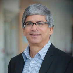 Professional headshot of a smiling man in a dark blazer and light blue shirt, wearing glasses.