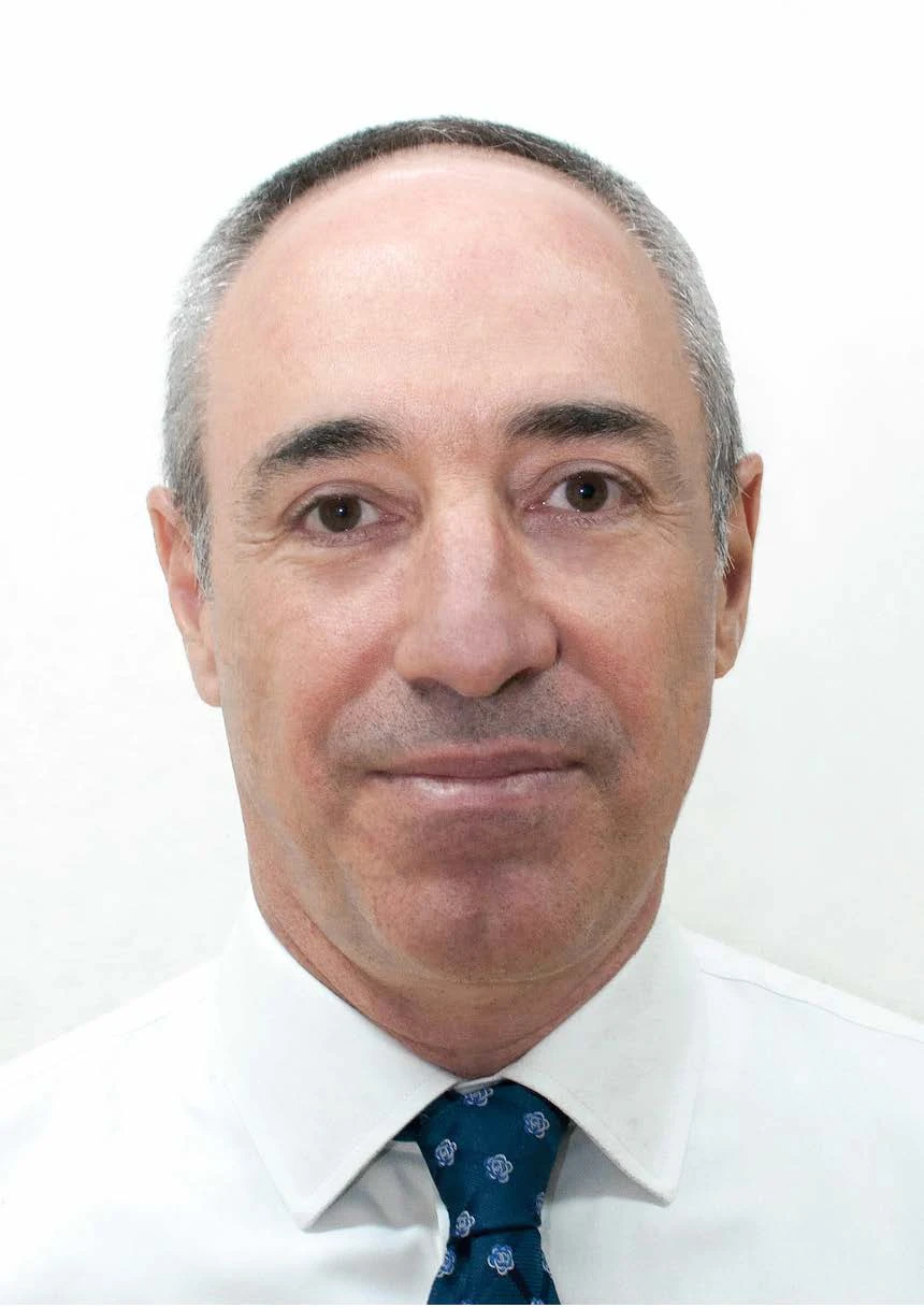 Professional head-and-shoulders portrait of a middle-aged man with short gray hair, wearing a white shirt and blue patterned tie, facing forward.