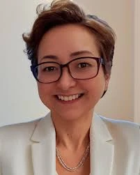 Smiling woman wearing glasses and a light blazer with short brown hair in a professional portrait surface.