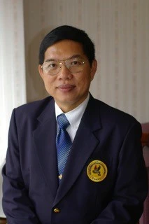 Professional portrait of a man in a dark suit and blue tie, wearing a circular gold badge on the left chest.