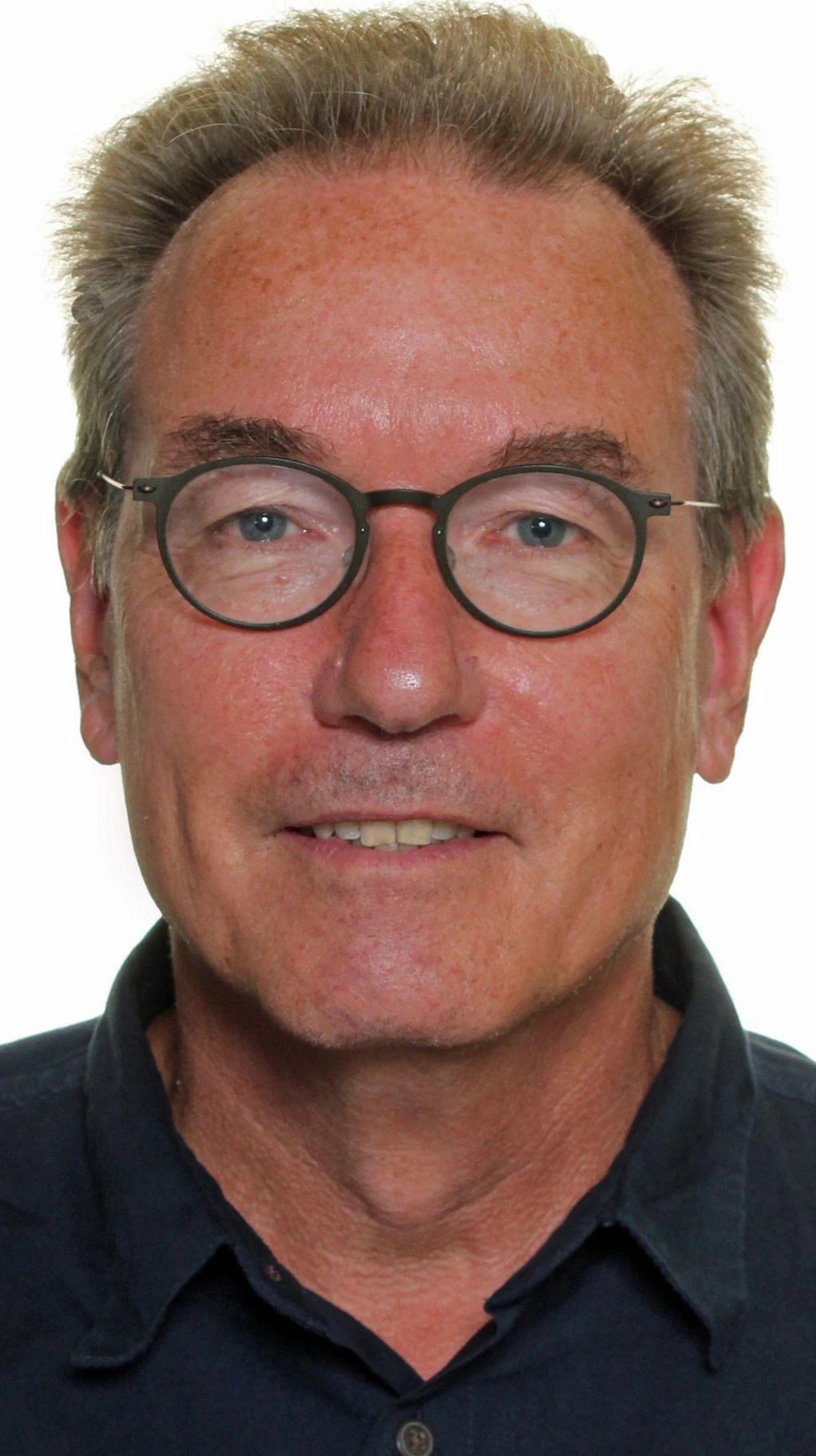 Man with short gray hair and round black glasses facing the camera, wearing a dark button-up shirt.
